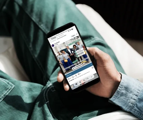 Hand hält ein Handy mit einer Instagram-Stellenanzeige für Anlagenmechaniker SHK in Düsseldorf